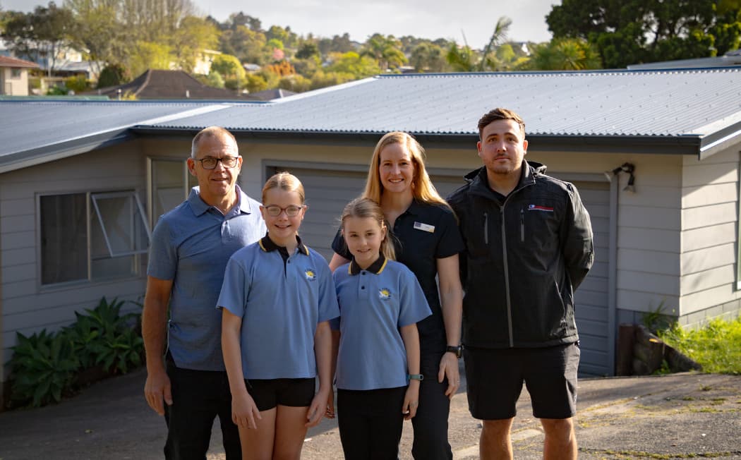 A family stands proudly in front of their residence, embodying togetherness and happiness in their home environment.