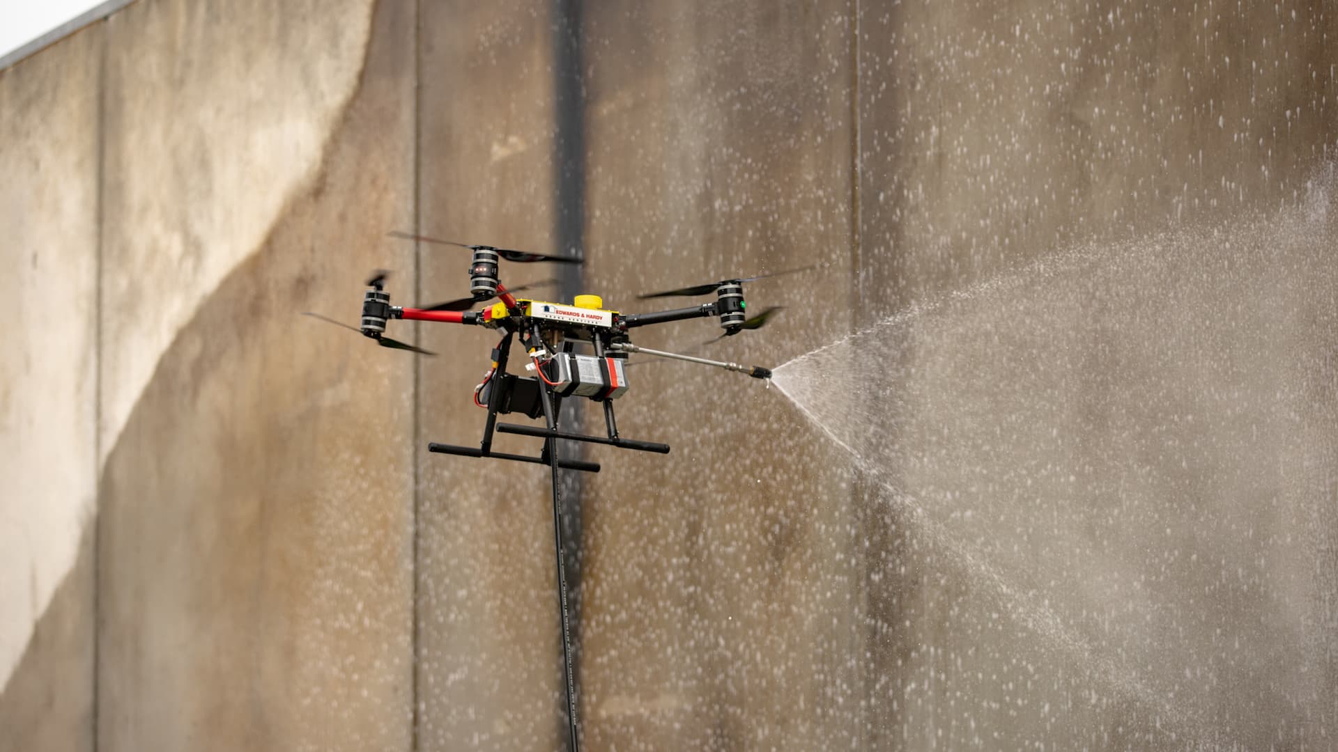 A drone spraying water on a wall for cleaning purposes.