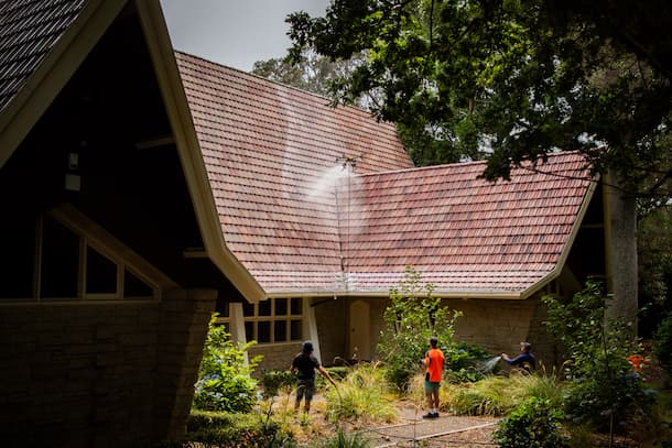 A group of people standing outside a house with a hose, while a drone sprays the roof.